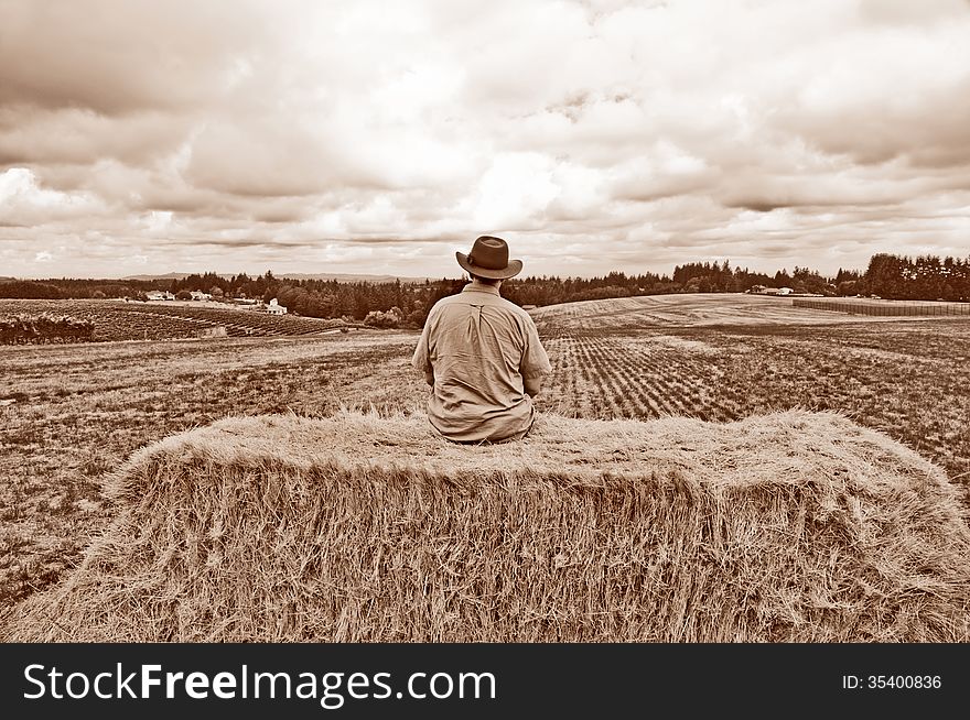 Man With Cowboy Hat Sitting On Bale Of Hay With Sepia Tone