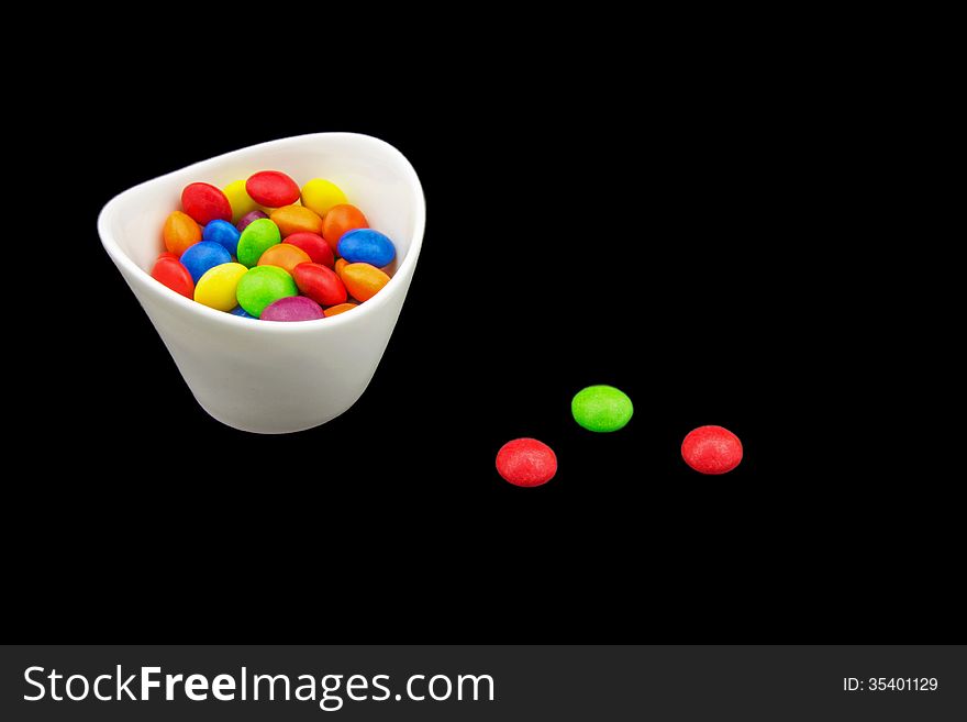 Multicolored candies in a bowl isolated on black background