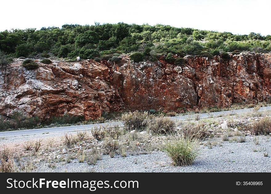 Its a road leading you through the Peloponnese. The rocky mountain stands out because of its red maroon color. Its a road leading you through the Peloponnese. The rocky mountain stands out because of its red maroon color.