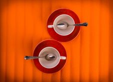Two White Empty Cups With Tea Spoons, On Red Plates Over Orange Color Background, View From Above Stock Photo Two White Empty Cups With Tea Spoons, On Red Plates Over Orange Color Background, View From Above Stock Photo