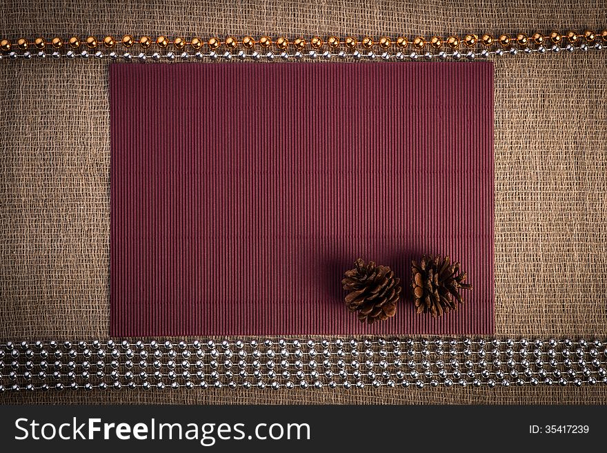 Horizontal blank greeting card. Light brown color linen background, claret paper, two pine cones and silver, golden color beads composition. Horizontal blank greeting card. Light brown color linen background, claret paper, two pine cones and silver, golden color beads composition.