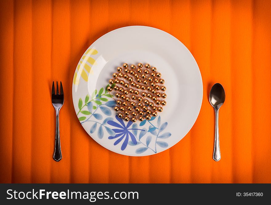 One lovely plate with golden beads on it , little fork and spoon by sides. Over textured bright orange color background. One lovely plate with golden beads on it , little fork and spoon by sides. Over textured bright orange color background.