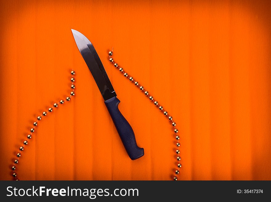 Knife cuts gold beads. Over textured bright orange color background.