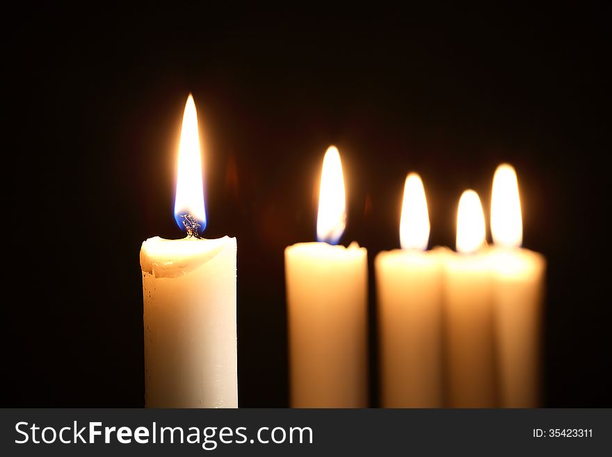 Five lighting candles in a row on dark background