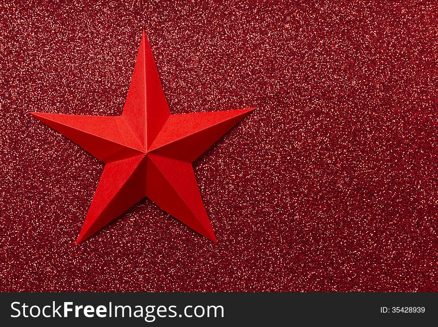 Paper origami star laying on colorful glitter background