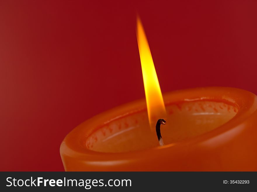 Candle with flame closeup on red background