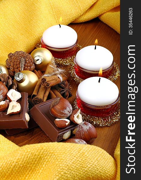 White candles with chocolate and hazelnuts on wood and yellow cloth. White candles with chocolate and hazelnuts on wood and yellow cloth