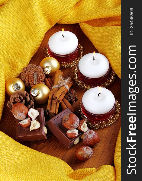 White candles with chocolate and hazelnuts on wood and yellow cloth. White candles with chocolate and hazelnuts on wood and yellow cloth