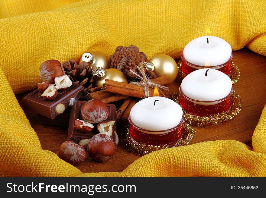 Hazelnuts, cinnamon, milk chocolate with Christmas balls on wood and outline of yellow cloth. Hazelnuts, cinnamon, milk chocolate with Christmas balls on wood and outline of yellow cloth