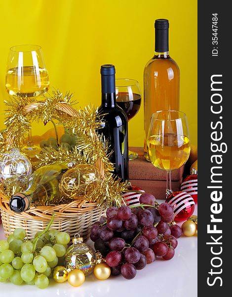 Bottles of wine with grapes and Christmas decorations on a white top and yellow cloth background. Bottles of wine with grapes and Christmas decorations on a white top and yellow cloth background