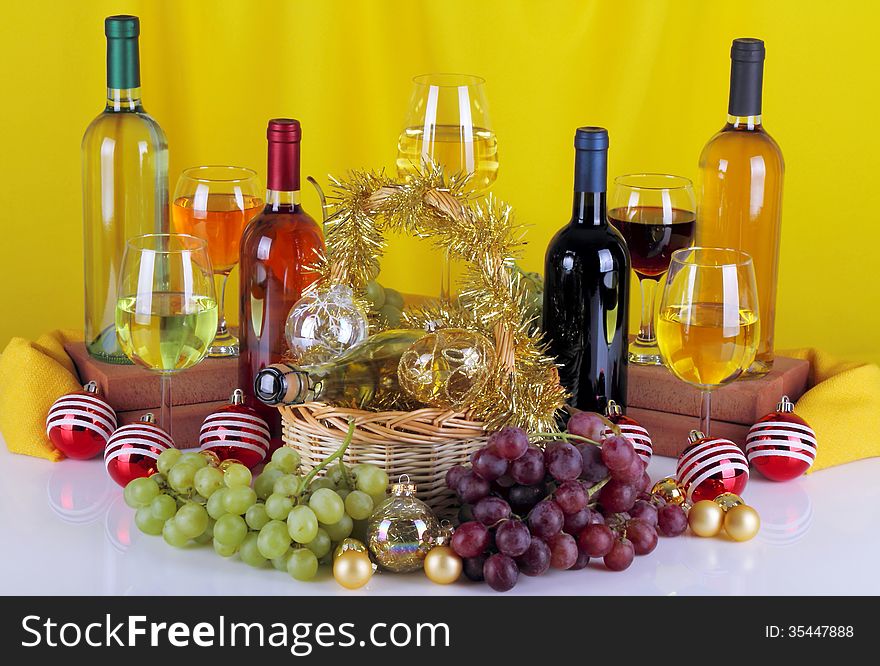 Bottles of wine with grapes and Christmas decorations on a white top and yellow cloth background