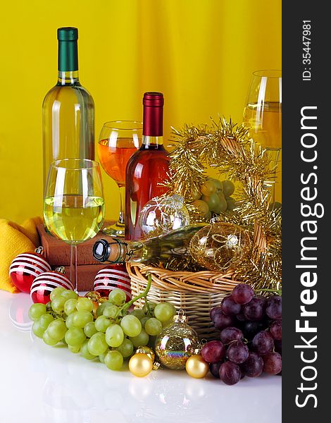 Bottles of wine with grapes and Christmas decorations on a white top and yellow cloth background