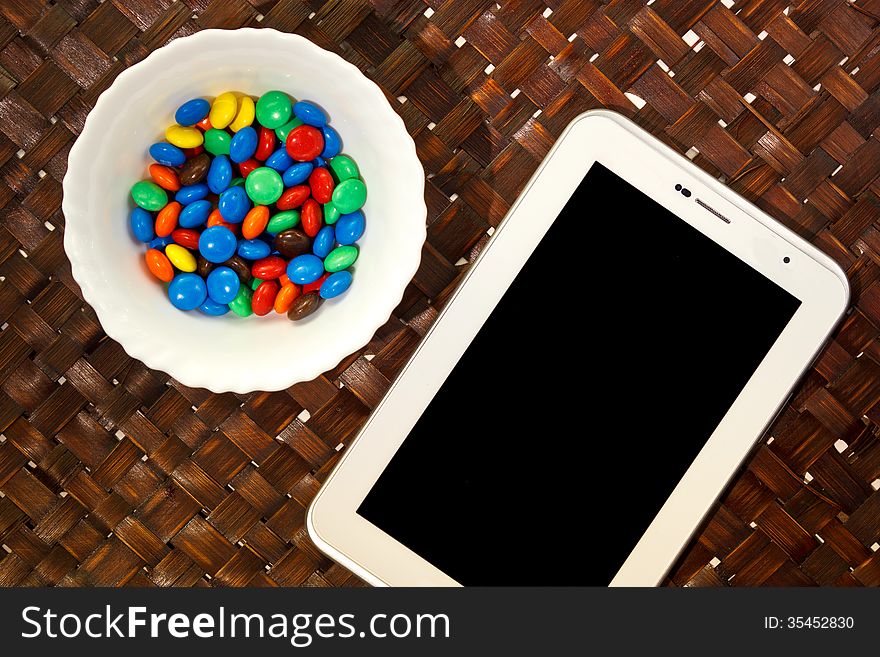 White touchscreen tablet and sweet colorful candy for coffee break. White touchscreen tablet and sweet colorful candy for coffee break