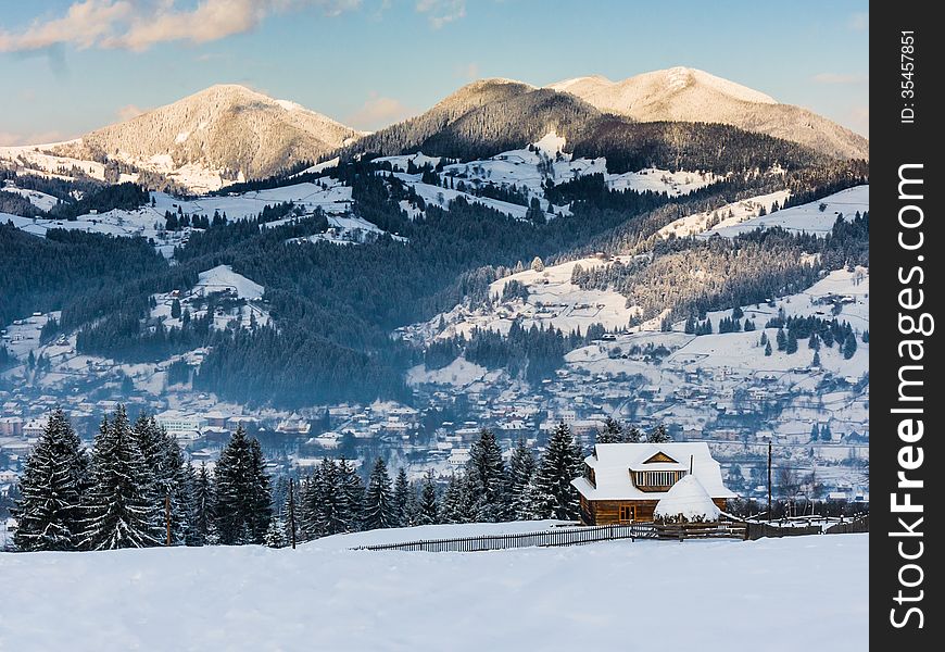 Winter landscape with a lonely cottage on a background of mountains