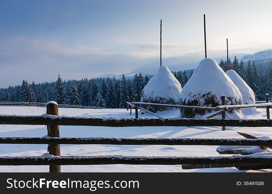 Three snow-covered haystacks and a fence in the foreground on the mountain top. Three snow-covered haystacks and a fence in the foreground on the mountain top