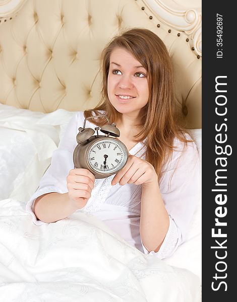 Young woman with alarmclock on the bed at the morning