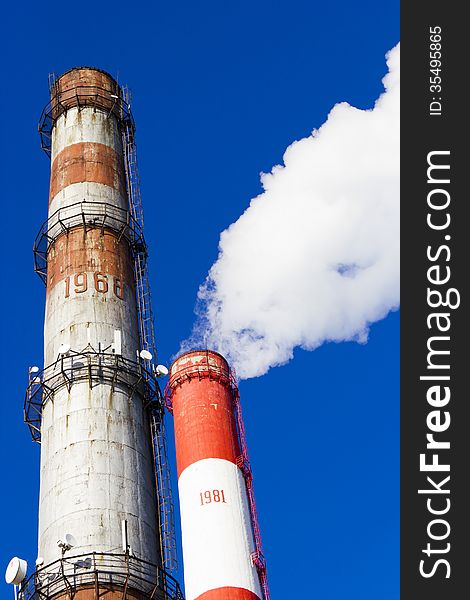 Pipes of power plant smoke against the bright blue sky. Pipes of power plant smoke against the bright blue sky