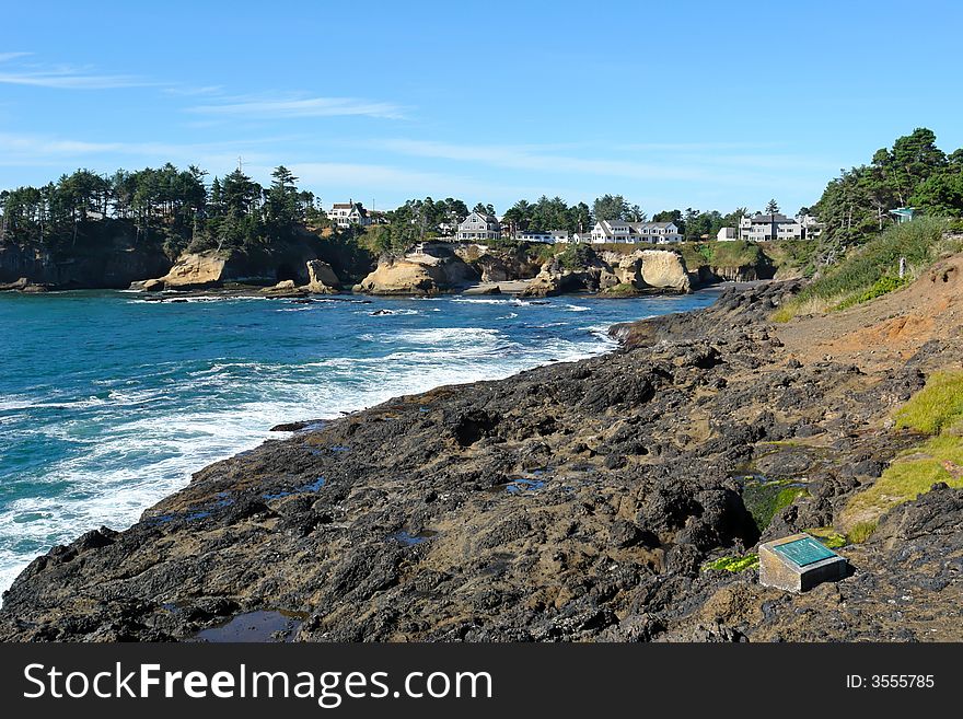 Scenic image of waves crashing on the oregon coast, with seagulls on the ledge and houses in the background. Scenic image of waves crashing on the oregon coast, with seagulls on the ledge and houses in the background