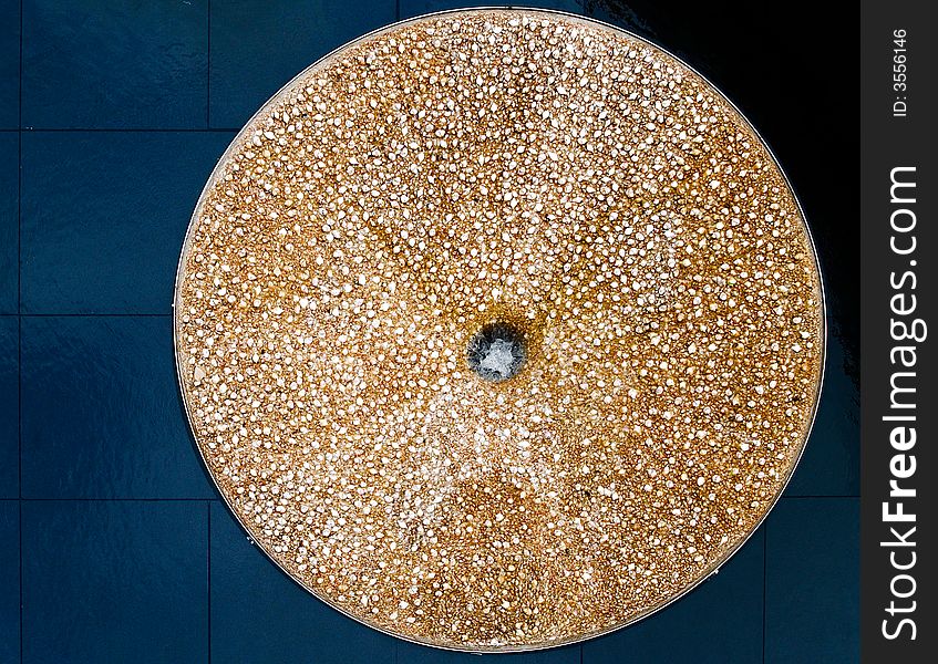 A circular shaped fountain encrusted with seashells on a black marble floor. A circular shaped fountain encrusted with seashells on a black marble floor