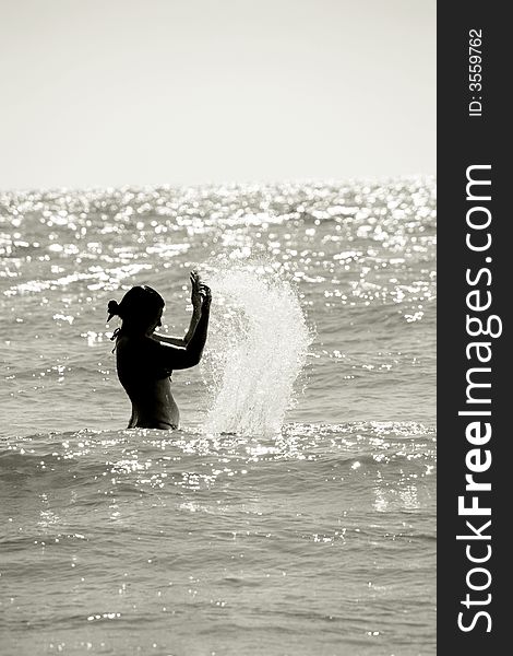 Silhouette of a wet young woman in a waving sea splashing the water, vertical. Silhouette of a wet young woman in a waving sea splashing the water, vertical