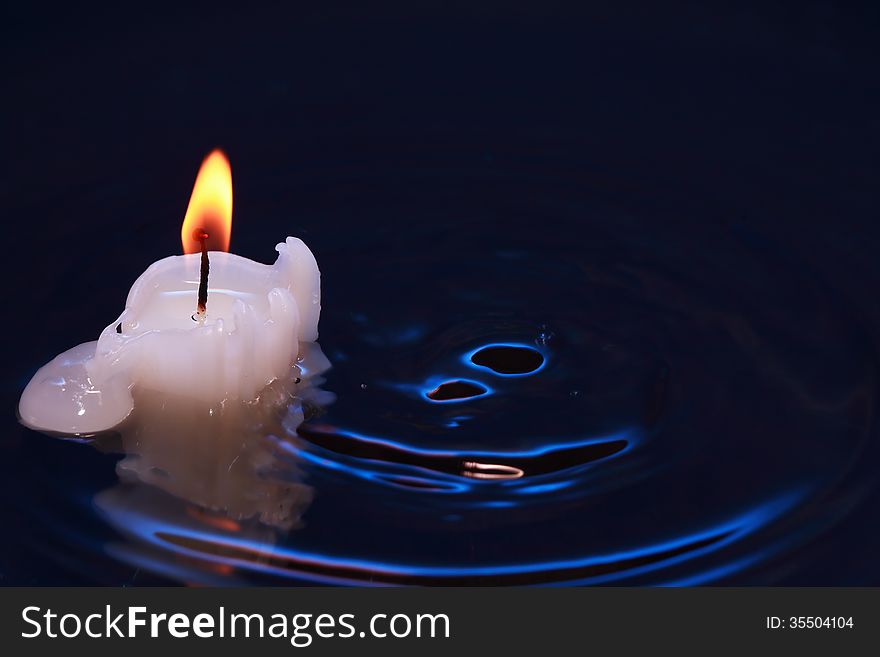 One lighting candle on dark splashing water surface. One lighting candle on dark splashing water surface
