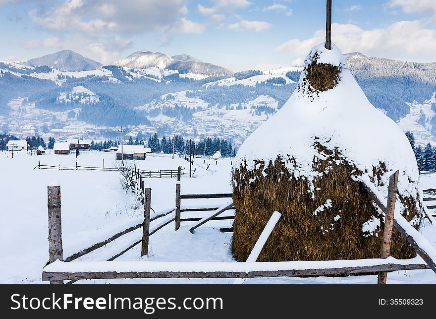 Snowy haystack and a fence on a background of a village and mountains. Snowy haystack and a fence on a background of a village and mountains