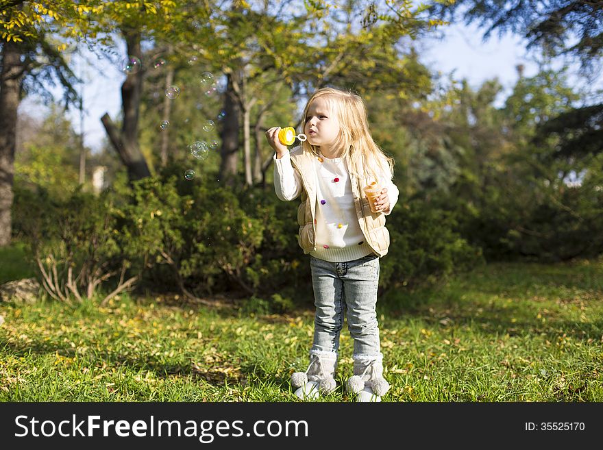 Funny little girl with soap bubbles in park