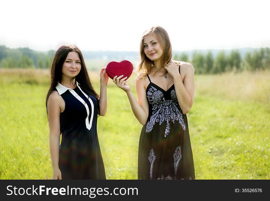 Two pretty women with red heart in sunshine summer field