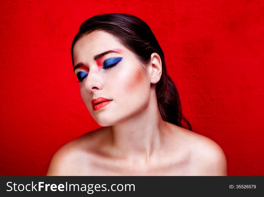 Beauty close up portrait of woman with colorful makeup on red backround