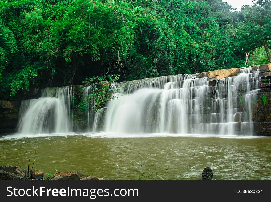 A beautiful waterfall with a green forest on the mountain