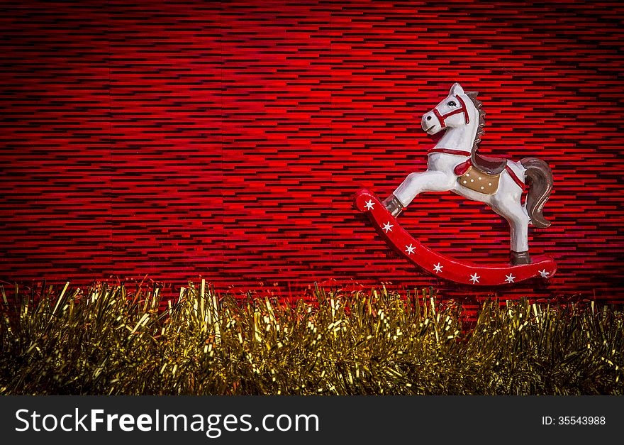 White color, rocking horse wooden toy over red color textured background with yellow sparkling garland at the bottom of composition. White color, rocking horse wooden toy over red color textured background with yellow sparkling garland at the bottom of composition.