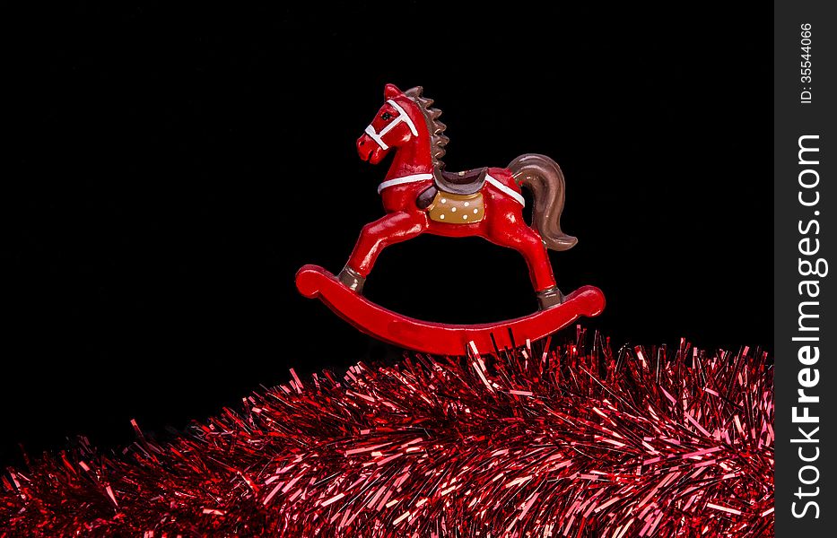 Red color rocking horse toy isolated over black color background, rocking above claret color textured sparkling garland at the bottom. Red color rocking horse toy isolated over black color background, rocking above claret color textured sparkling garland at the bottom.