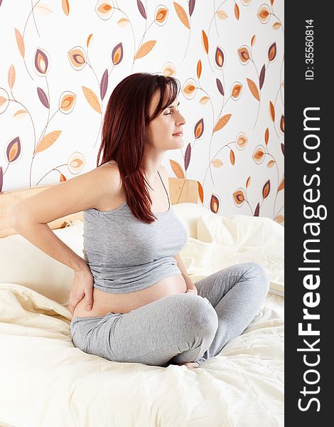 Pregnant woman kneeling on bed with hands on hips suffering from backache. Pregnant woman kneeling on bed with hands on hips suffering from backache.