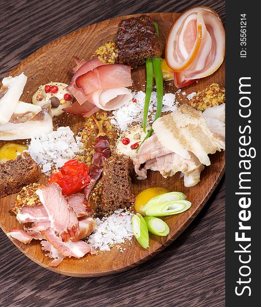 Wooden Plate with Various Smoked, Boiled and Uncooked Ham, Mustard, Salt, Brown Bread and Spices on Dark Wooden background. Wooden Plate with Various Smoked, Boiled and Uncooked Ham, Mustard, Salt, Brown Bread and Spices on Dark Wooden background