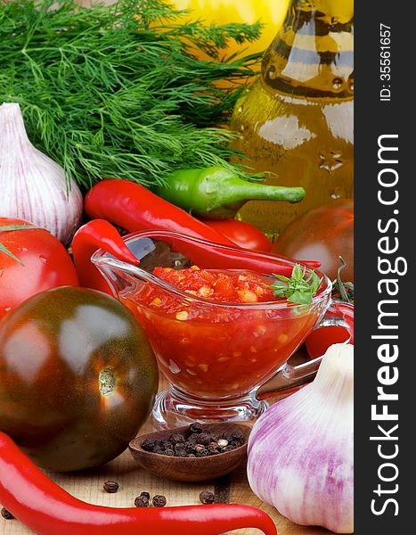 Arrangement of Bruschetta Sauce in Glass Gravy Boat with Black Tomatoes, Garlic, Chili Peppers and Olive Oil in Glass Bottle closeup on Wooden background