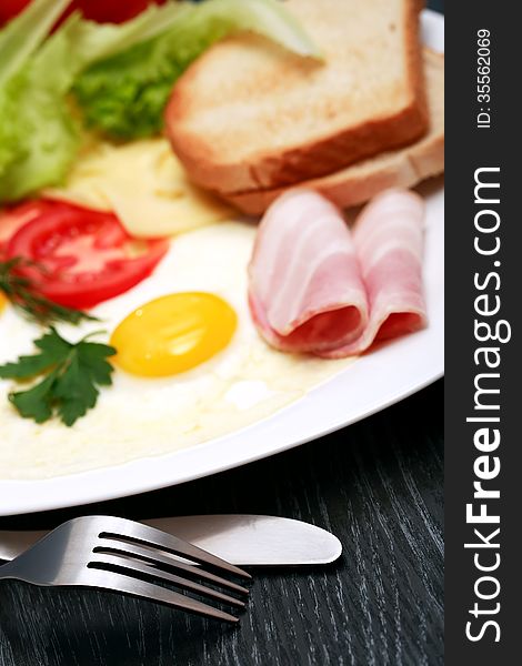 Closeup of fork and knife near plate with fried eggs, toasts and cheese