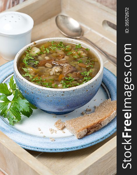 Bowl of mushroom soup with pearl barley on a wooden tray, vertical