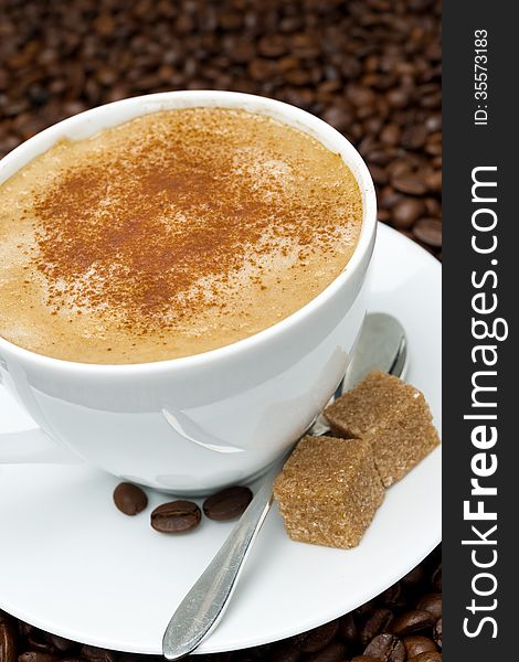 Cup of cappuccino with brown sugar on the background of coffee beans, close-up, vertical