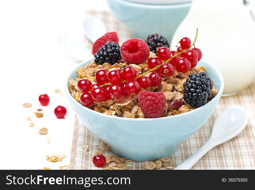 Delicious granola in the bowl with fresh berries and jug of milk, isolated on white