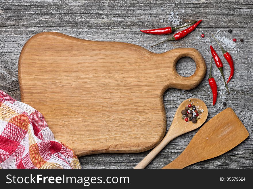 Figured wooden cutting board, spoon, spatula and spices, space for recipe, top view, horizontal