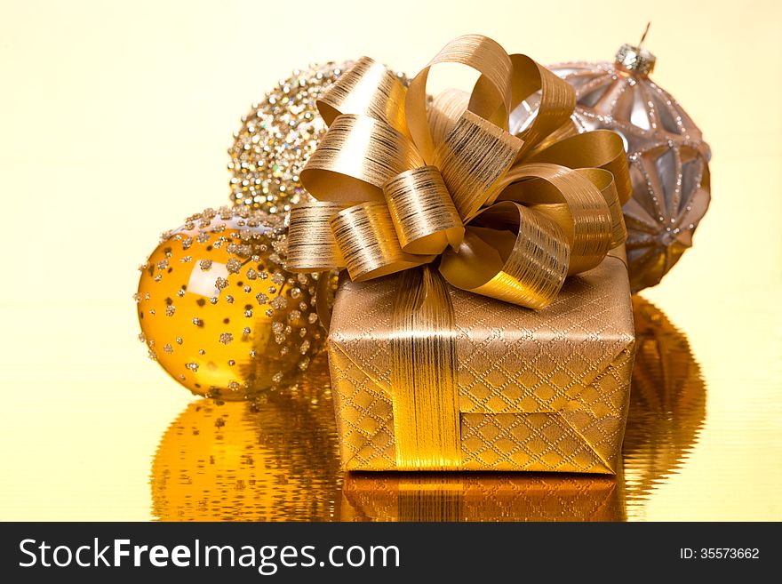 Gift box and Christmas balls on golden background, close-up