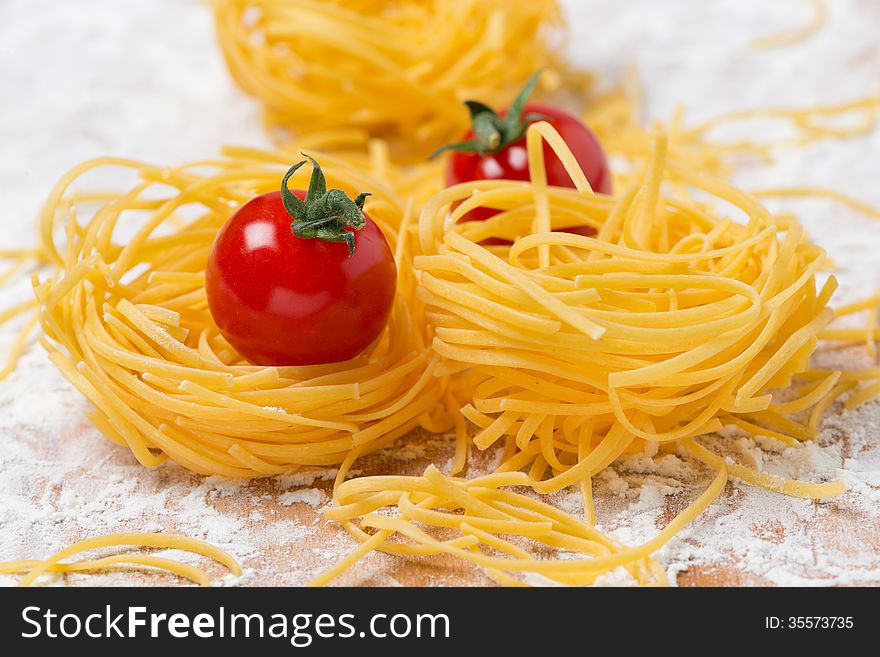 Italian egg pasta nest, cherry tomatoes on a cutting board sprinkled with flour, close-up. Italian egg pasta nest, cherry tomatoes on a cutting board sprinkled with flour, close-up