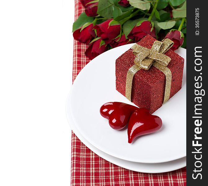 Red gift box and two hearts on a plate, roses in the background