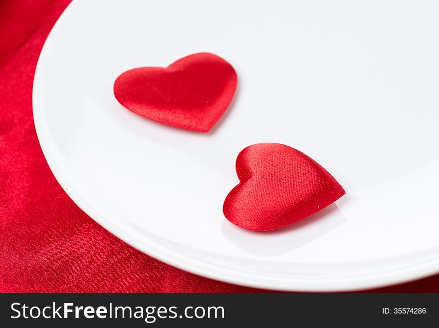 Two silk heart on a plate on red background, selective focus, close-up