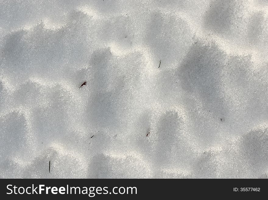 Shiny snow close up with shadows and small pieces of grass poking through. Shiny snow close up with shadows and small pieces of grass poking through