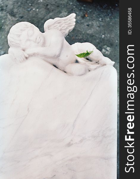 Angel cut from white marble, the green leaf lies on a foot of an angel. Angel cut from white marble, the green leaf lies on a foot of an angel