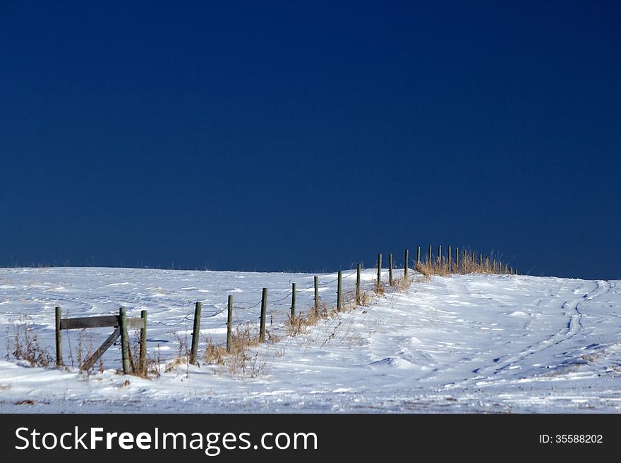 A fence line going uphill on a snow covered ground and a blue sky. A fence line going uphill on a snow covered ground and a blue sky