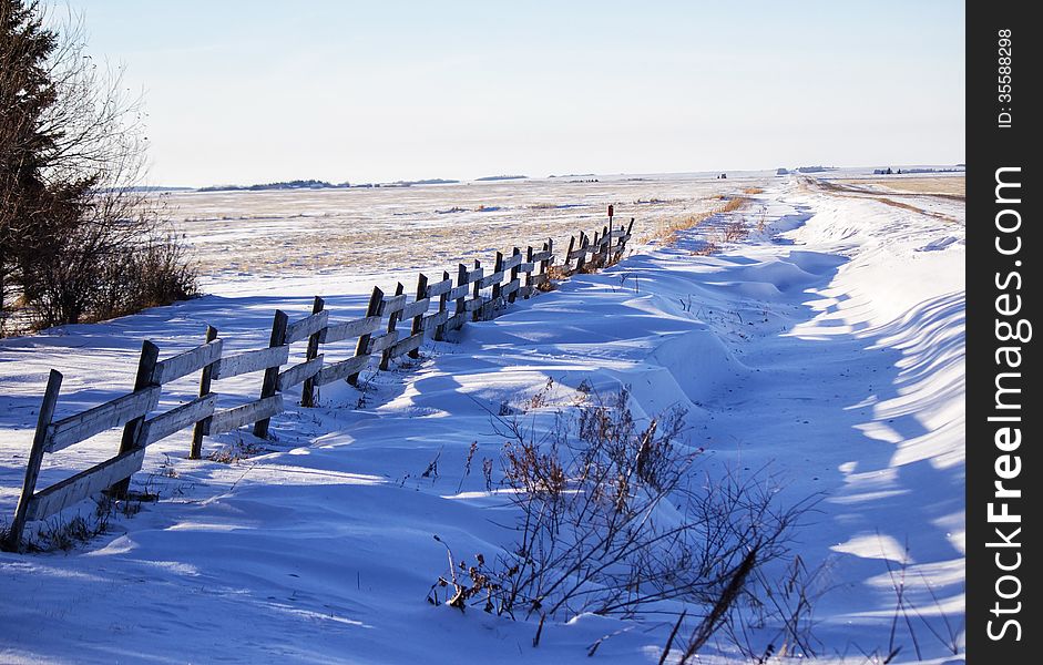 Wood fence along a ditch with snow drifts. Wood fence along a ditch with snow drifts