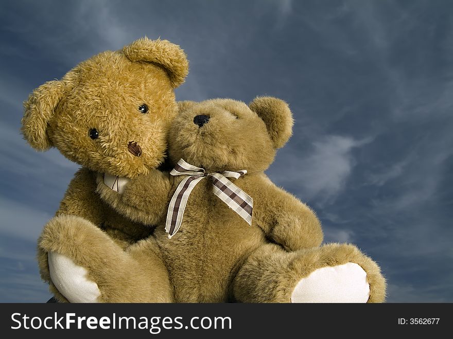 Two teddy bears hugging each other agaist blue sky with cirrus clouds. Two teddy bears hugging each other agaist blue sky with cirrus clouds