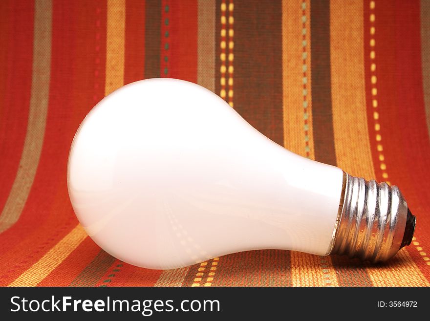 Close up side-view of a white light bulb against colorful background.